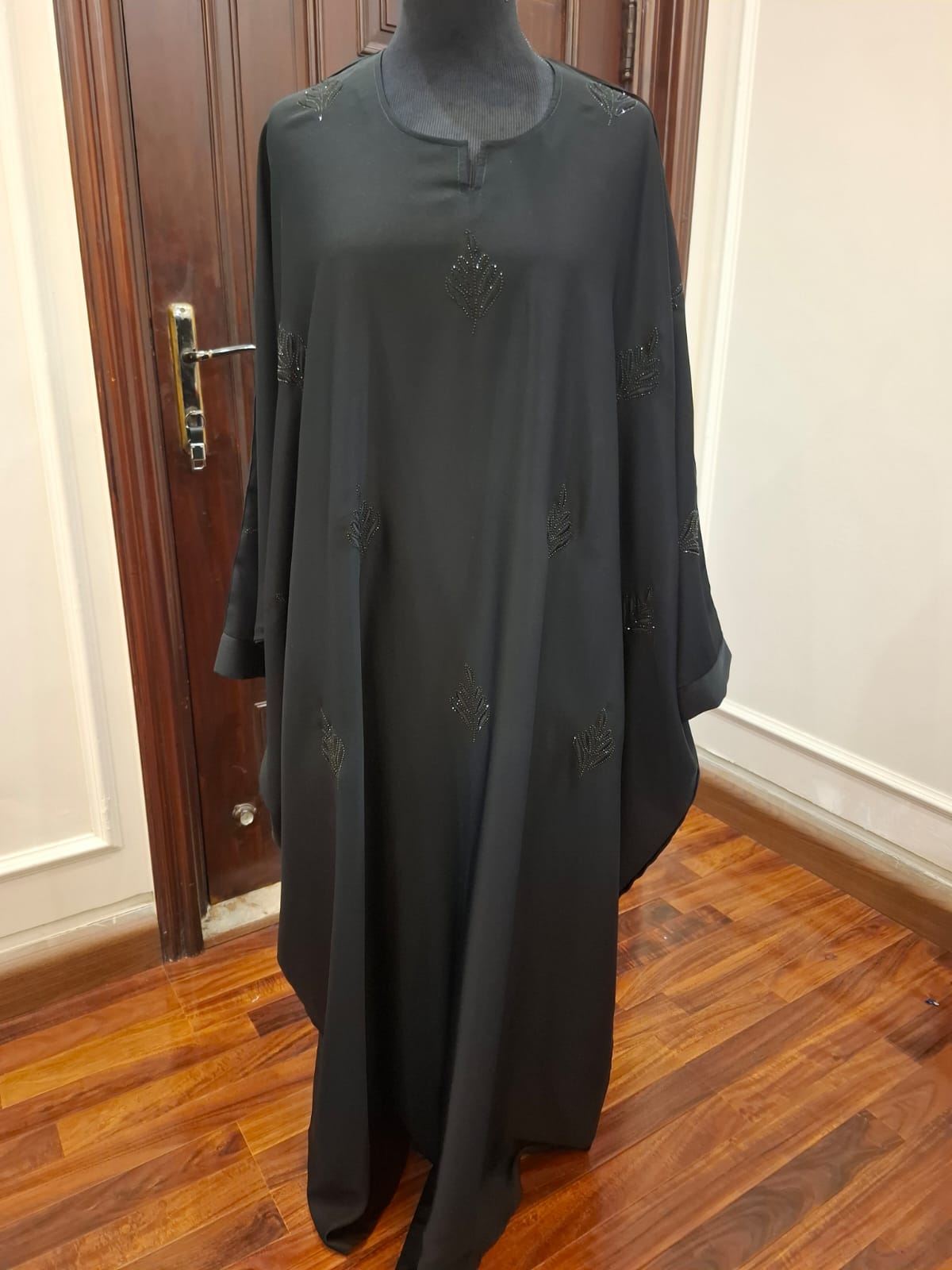 Black dress on a mannequin against a wooden door and floor.