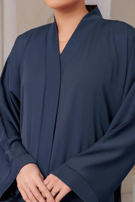 Person wearing a dark blue abaya with a neutral background