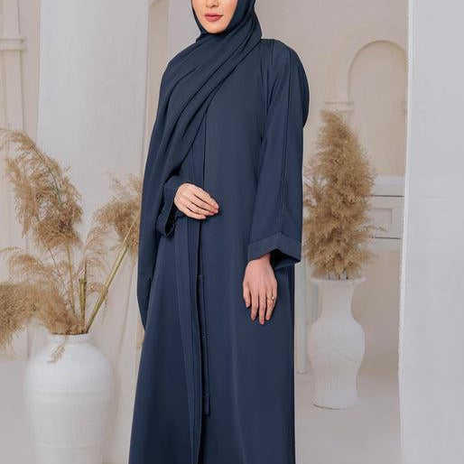 Woman wearing a dark blue abaya in an elegant indoor setting with decorative plants and a patterned rug.