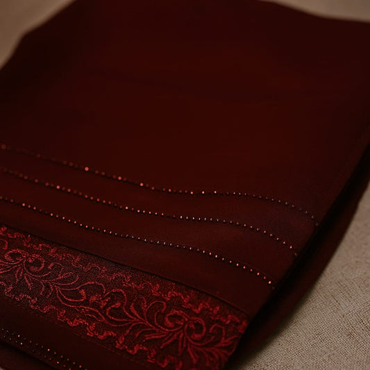 Close-up of a dark red fabric with intricate stitching and lace trim on a neutral background