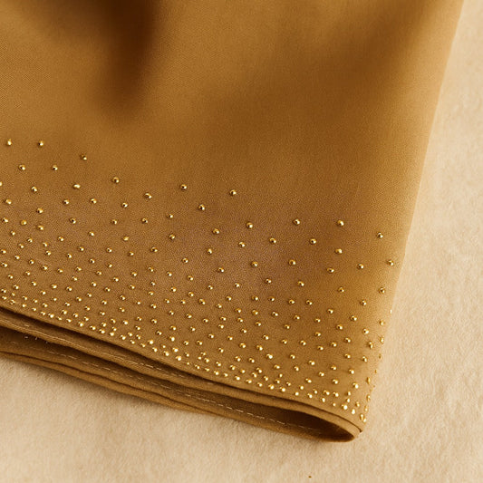 Close-up of a folded piece of brown fabric with small gold studs on a beige background